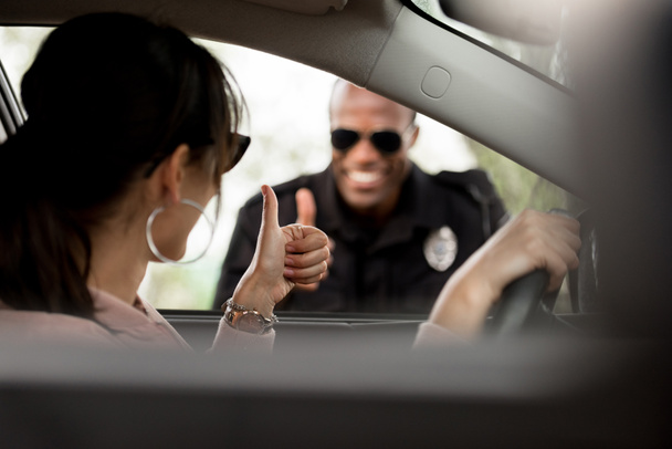 Young female driver in car and smiling policeman doing thumb up gesture to each other - Фото, изображение