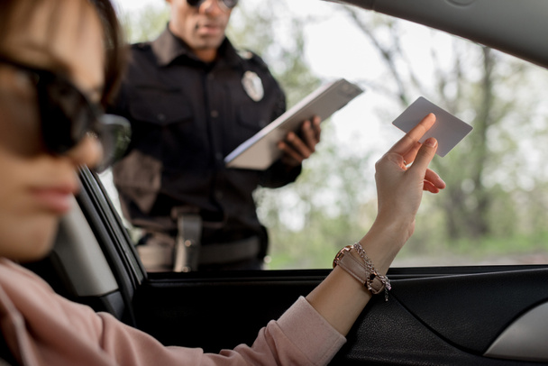 Žena v sluneční brýle sedí v autě a dávat řidičský průkaz policista  - Fotografie, Obrázek