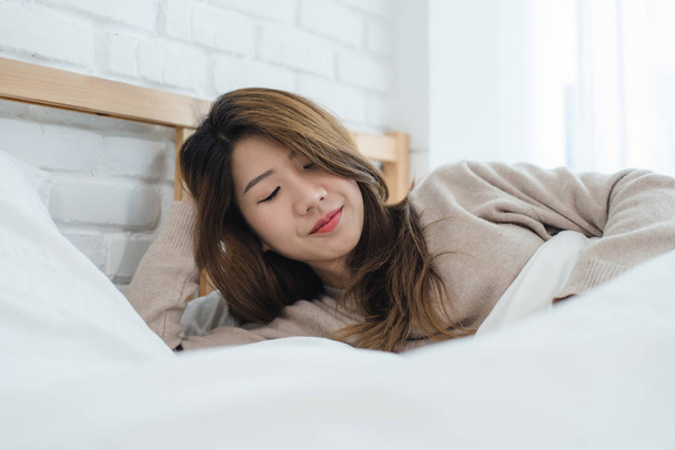 Muotokuva kaunis nuori aasialainen nainen sängyssä kotona aamulla. Iloinen aasialainen nainen yllään mukava villapaita ja hymyilee sängyllään. Rentoutumishuone. elämäntapa Aasia nainen kotona käsite
. - Valokuva, kuva