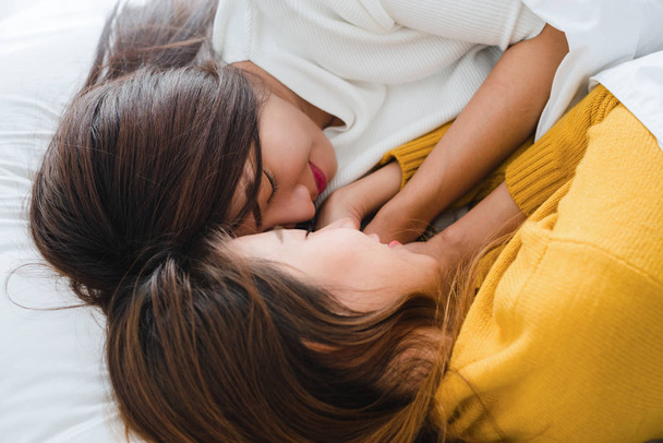 schöne junge asiatische Frauen lgbt lesbische glückliche Paar umarmen und lächeln, während sie zusammen im Bett unter Decke zu Hause liegen. Lustige Frauen nach dem Aufwachen. lgbt lesbisches Paar zusammen drinnen Konzept. - Foto, Bild
