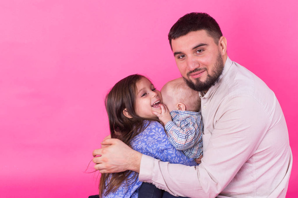 ピンクの背景に彼の幼い娘と赤ちゃんの息子を運ぶハンサムな父親 - 写真・画像