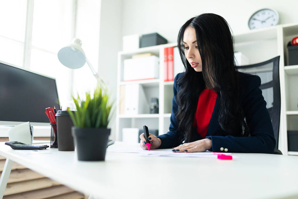 Beautiful young girl is working with documents in the office at the table. The girl highlights important points in the document with a pink marker. - 写真・画像