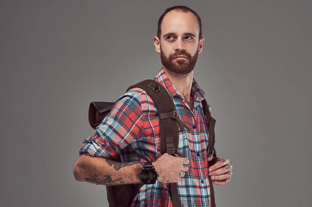Portrait of a handsome tattooed traveler in a flannel shirt with a backpack, standing in a studio. - Photo, Image