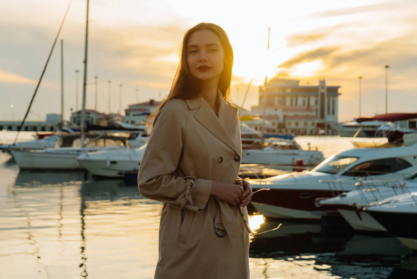 attractive long haired woman in coat posing by the sea in evening sun, smile - Valokuva, kuva