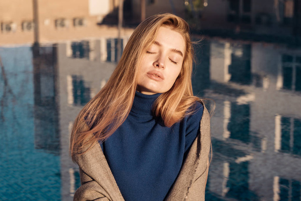 beautiful blonde girl sits by the blue pool in the sun, closes her eyes and rests - Foto, immagini