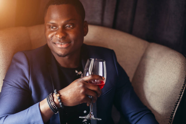 Portrait of handsome afroamerican man in blue jacket drinking wine at restaurant - Zdjęcie, obraz