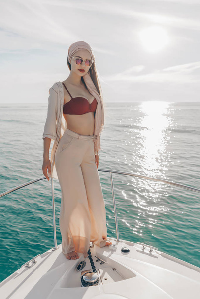 beautiful rich woman in summer clothes and sunglasses stands on a white yacht, enjoys vacation and sea - Foto, Imagem