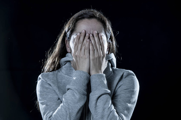 concept of fear, shame, violence and depression. Attractive latin depressed woman covers her face with her hands on a isolated black background - Foto, immagini