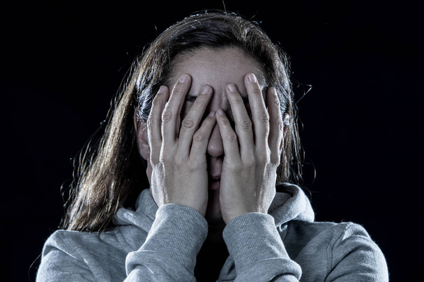concept of fear, shame, violence and depression. Attractive latin depressed woman covers her face with her hands on a isolated black background - 写真・画像