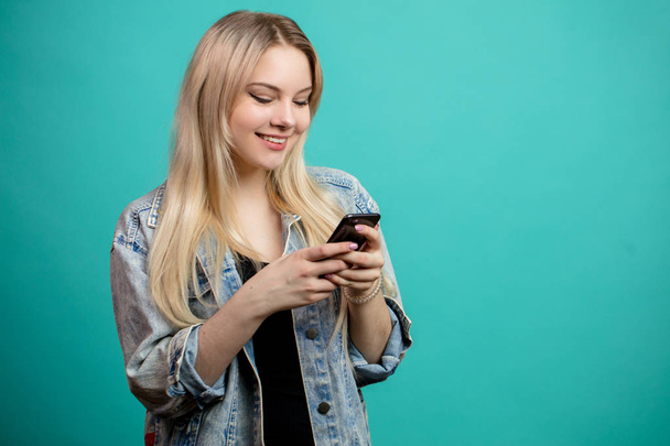 Cheerful young caucasian female using smartphone on blue - Фото, изображение
