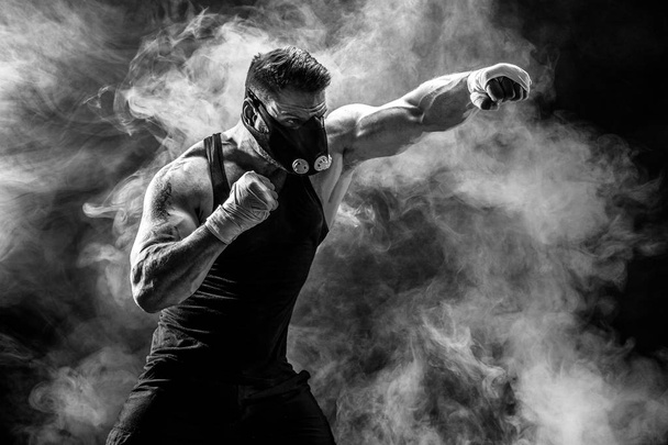 Strong male athlete in a black training mask on a black background - 写真・画像
