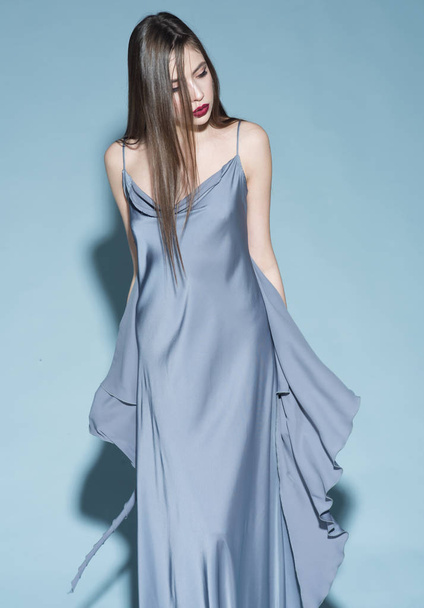 Fashion concept. Girl on strict confident face in long blue dress, light blue background. Lady with red lips wears beautiful dress. Woman, fashion model with stylish makeup and hairstyle. - Photo, Image