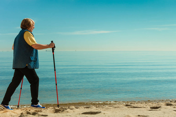 Senior woman practicing nordic walking on beach - Fotoğraf, Görsel