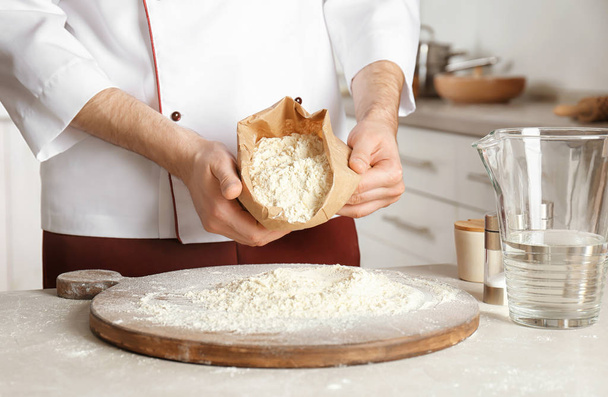 Chef masculino esvaziando farinha fora do pacote de papel a bordo na cozinha
 - Foto, Imagem