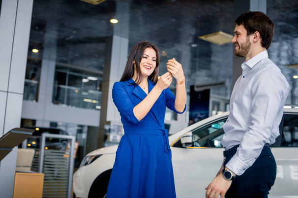 Happy beautiful woman receiving keys from a new car at auto showroom - 写真・画像