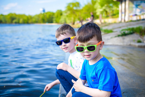 Enfants jouant à l'extérieur dans la nature : assis sur le bord d'un lac ou d'une rivière touchant du sable en eau claire pendant les chaudes journées d'été ou de printemps
. - Photo, image