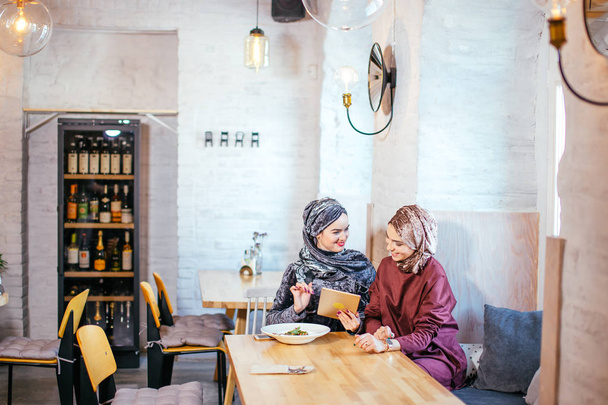 Two Muslim women in cafe, shop online using electronic tablet - Photo, image