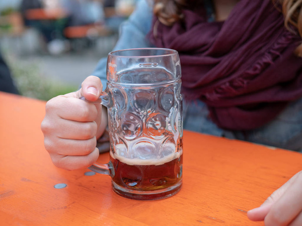 テーブルの上の女性によって開催されたドイツのビールのほとんど空のグラス  - 写真・画像