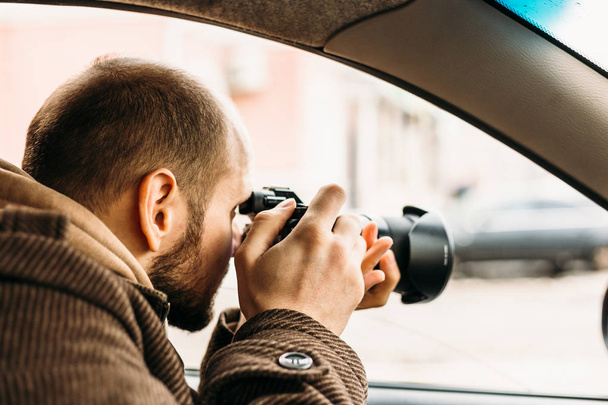 Private detective or reporter or paparazzi sitting in car and taking photo with professional camera - Фото, изображение