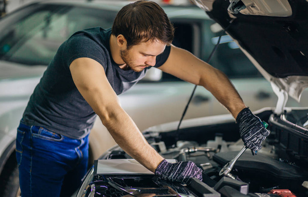mechanic working under car hood in repair garage - Fotografie, Obrázek