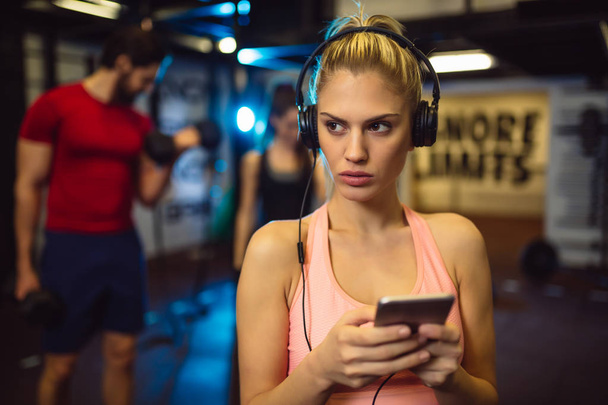 Mujer rubia joven escuchando música favorita en los auriculares en el gimnasio
 - Foto, Imagen