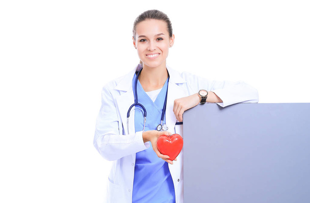 Médica feminina positiva em pé com estetoscópio e símbolo de coração vermelho
 - Foto, Imagem