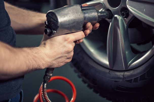 mechanic screwing or unscrewing car wheel by pneumatic wrench - 写真・画像