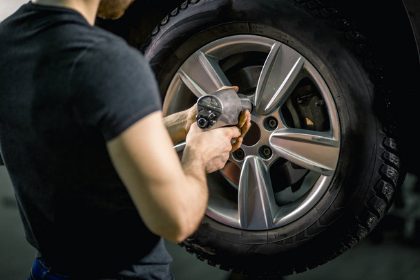 mechanic screwing or unscrewing car wheel by pneumatic wrench - Foto, Bild