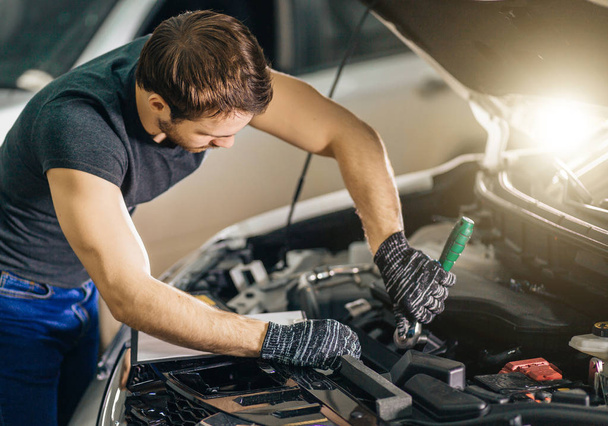 mechanic working under car hood in repair garage - Foto, immagini