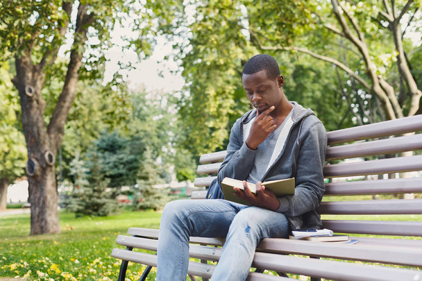 Young man reading book in park copy space - Фото, изображение