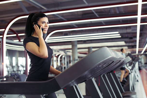 woman smiling while talking on mobile phone while running on treadmill - 写真・画像
