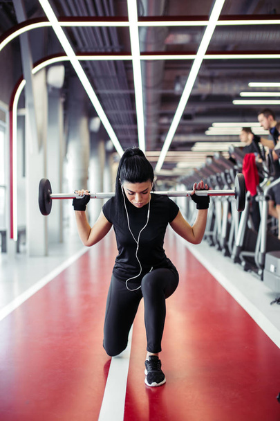 girl doing lunges with barbell in modern gym - Photo, Image