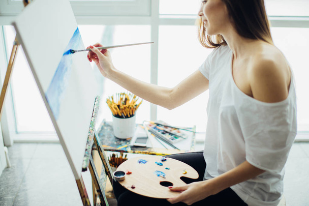 Woman artist painting a picture in a well-lit studio - Φωτογραφία, εικόνα