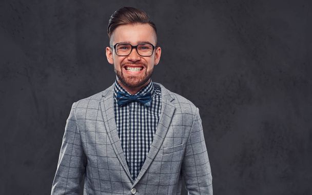 Homem barbudo elegante confiante com penteado em um terno cinza retro elegante e gravata borboleta, posando em um estúdio
. - Foto, Imagem