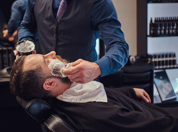 Usta Kuaför yüz tıraş için hazırlar ve yüzü bir kuaför salonu olarak köpük ile smear. - Fotoğraf, Görsel