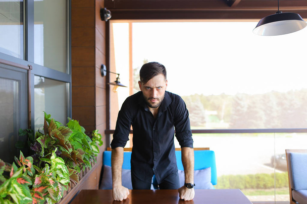 Gestionnaire masculin caucasien debout au bureau et portant une chemise noire
. - Photo, image