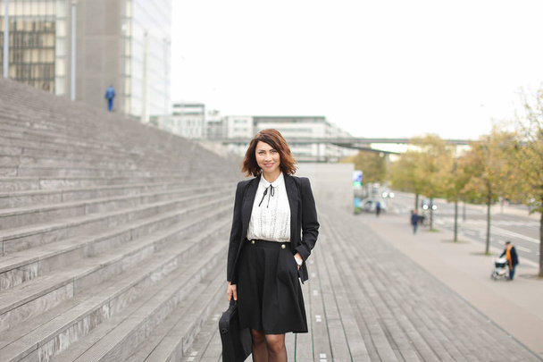 Female manager standing on stairs outside in high buildings background. - Foto, Bild