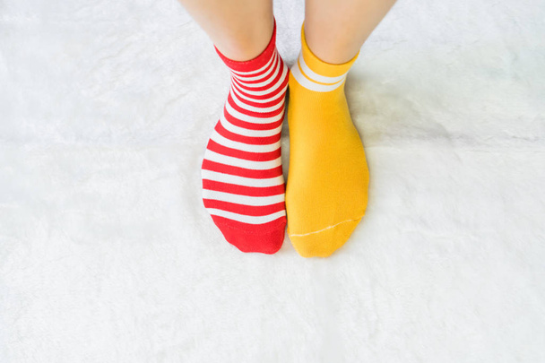 Lábát a zokni két szín alternatív, piros és sárga oldalon állni a padló fehér szövet. - Fotó, kép