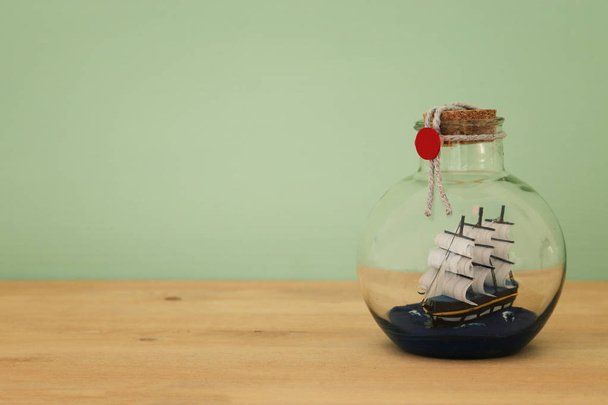 nautical concept image with sail boat in the bottle over wooden table. Selective focus - Фото, изображение