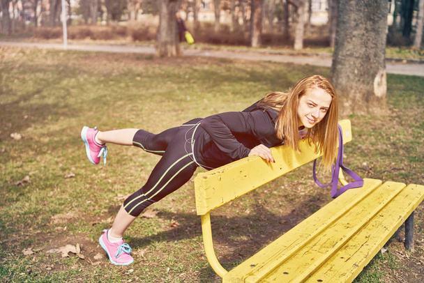 Beautiful sportswoman with smartphone exercising in park - Photo, Image