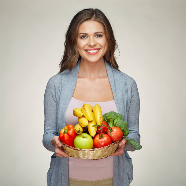 smiling woman holding straw basket with vegetables and fruits on light background, close-up  - Photo, image