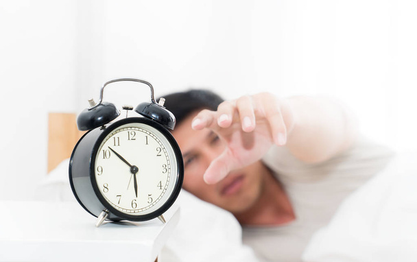 Man's hand is reaching out to alarm clock waking up in early mor - Photo, Image