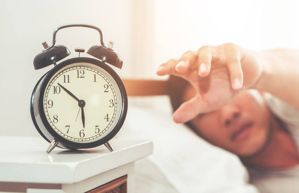 Man's hand is reaching out to alarm clock waking up in early morning - Photo, Image