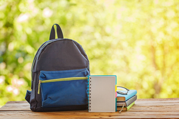 School backpack with books on wooden table and nature background - Фото, зображення
