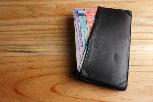 Lederen mannen open portemonnee met Maleisië bankbiljetten en credit card binnen op een houten achtergrond. - Foto, afbeelding