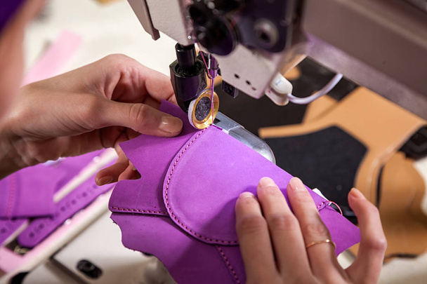 Крупный план молодой женщины, работающей швеей в фиолетовом мундире, шьет настоящие кожаные детские туфли на швейной машинке
 - Фото, изображение