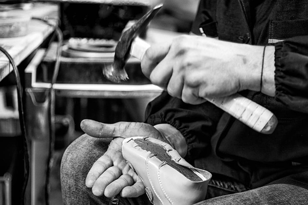 Close-up of a young man worker in jeans makes a soles of children's shoes made of genuine leather, clogs nails in a sewing workshop - Photo, Image