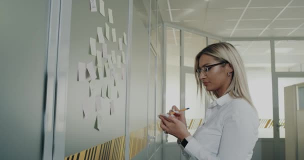 オフィス、いくつかの仕事の計画を作る労働者の女性と男性とオフィスの壁に貼り付けて - 映像、動画