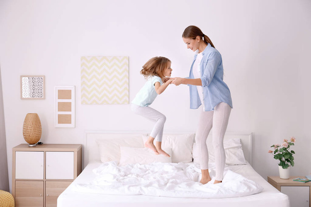 Happy mother and her daughter jumping on bed in children room - Foto, Imagem