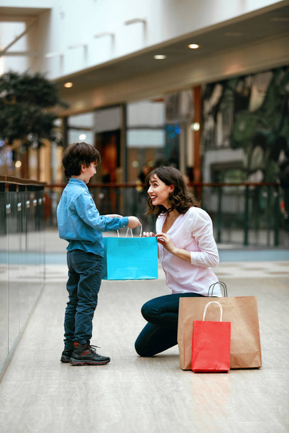 Shopping Centre. Child Giving Presents To Mother - Фото, изображение